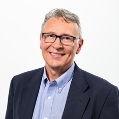 a man with glasses in a suit smiling at camera